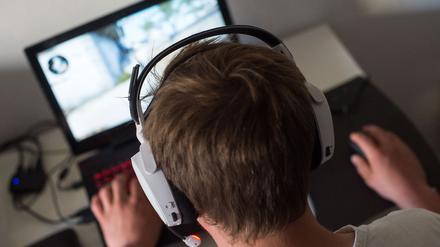 Ein Mann sitzt mit einem Headset vor einem Laptop und spielt ein Online-Computerspiel.