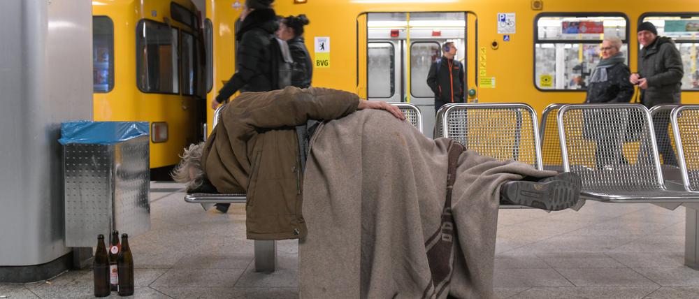 Ein obdachloser Mensch schläft auf einer Bank in einem Berliner U-Bahnhof. Neben ihm stehen leere Bierflaschen. (Symbolbild)
