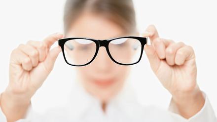 Eine Frau hält eine Brille mit beiden Händen vor ihr Gesicht.