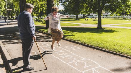 Ein Rentnerpaar spielt Himmel und Hölle in einem Park.
