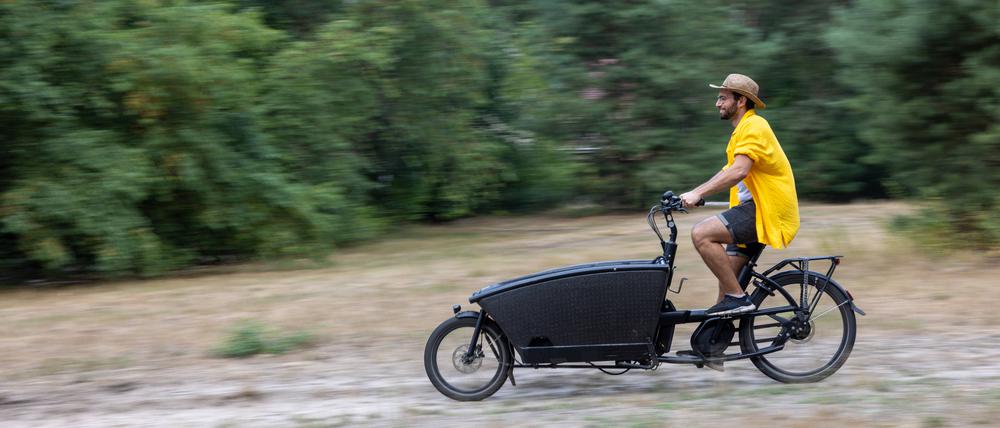 Ein junger Mann fährt über eine Wiese mit seinem elektrisch betriebenen Lastenrad.