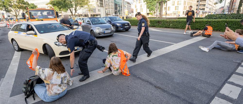 Polizisten rennen auf der Kreuzung am Stachus in der Innenstadt zu Teilnehmern· der Letzten Generation“, die sich zuvor festgeklebt haben. 