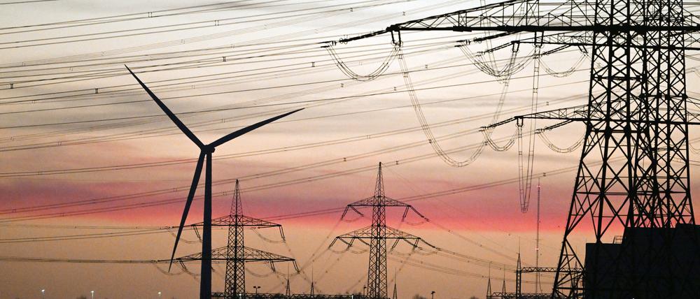 ARCHIV - 26.02.2022, Nordrhein-Westfalen, Rommerskirchen: Strommasten und Windräder stehen nach Sonnenuntergang im letzten Licht der Dämmerung da. Verbraucher sollen nach dem Willen der EU-Kommission mit Einnahmen aus übermäßigen Gewinnen von Energiefirmen entlastet werden. (zu dpa «EU-Kommission will übermäßige Gewinne von Energiefirmen abschöpfen») Foto: Federico Gambarini/dpa +++ dpa-Bildfunk +++
