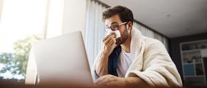 Shot of a sickly young businessman blowing his nose with a tissue while working from home