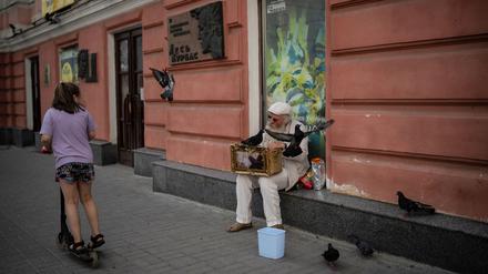 Alltagsszenen aus Charkiw: Ein Mädchen fährt auf einem Roller die Straße herunter, ein Mann füttert Tauben.