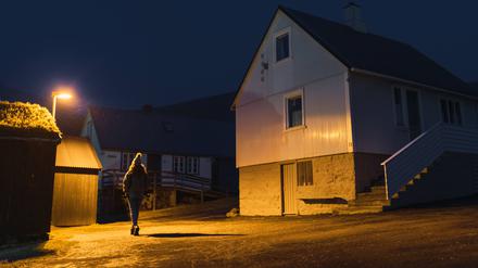 Eine Frau läuft nachts in einer Straße eines kleinen Dorfes entlang.