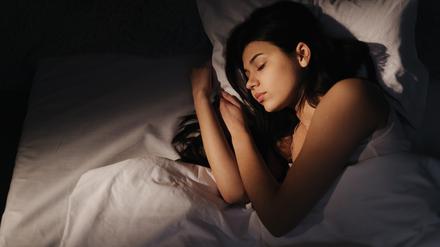 Eine Frau mit dunklen Haaren schläft nachts in einem Bett mit weißer Bettwäsche. 