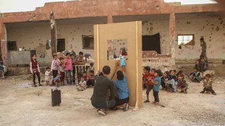 Ein Puppenspiel vor einer zerstörten Schule in Syrien, die vertrieben Kindern als Unterkunft dient. 