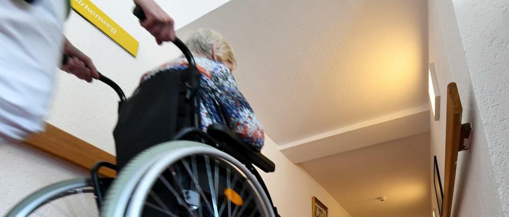 Eine Pflegerin schiebt eine ältere Dame im Rollstuhl über einen Flur in einem Seniorenpflegeheim.