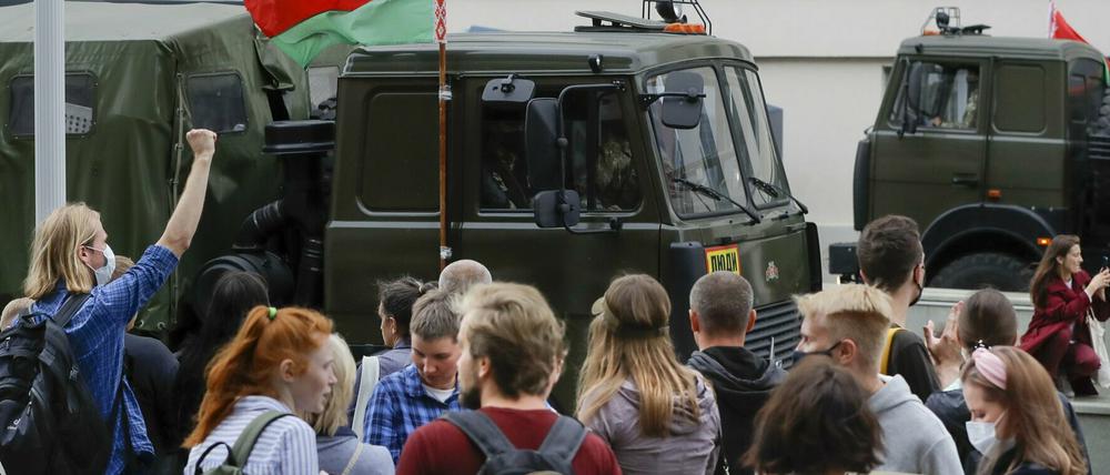 Demonstranten in Minsk stehen vor Polizeifahrzeugen.