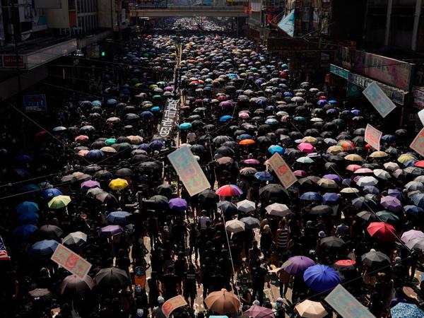  Teilnehmer einer Demonstration marschieren, zumeist schwarz gekleidet, mit Regenschirmen durch Hongkong.
