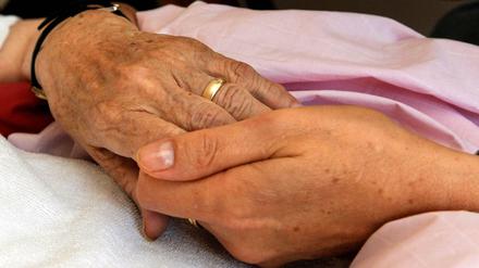 Eine Schwester hält die Hand einer todkranken Bewohnerin eines Hospizes.