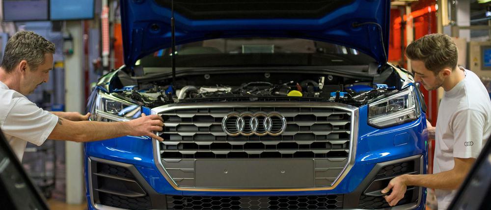 Zwei Fertigungsmechaniker bringen an einem Fließband im Audi-Werk das Frontende an einem Audi an.