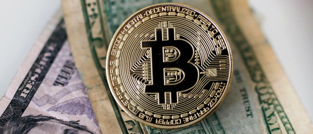 Archivbild einer Bitcoin Münze, die auf einem Dollar Geldscheinen liegt (gestellte Szene).