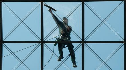 Ein Gebäudereiniger putzt in 27 Meter höhe ein gläsernes Dach.