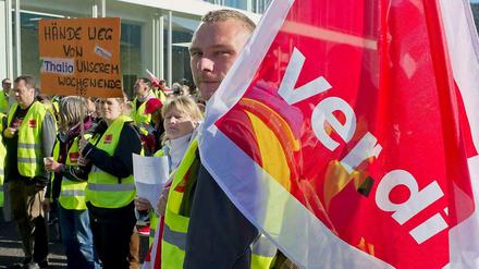 Ein Verdi-Mitglied trägt eine Fahne seiner Gewerkschaft auf der Schulter und steht zusammen mit anderen Beschäftigten vor einem Gebäude.