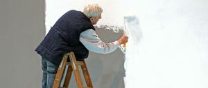 Ein älterer Herr mit grauen Haaren weißt eine Wand auf der Leipziger Messe. 