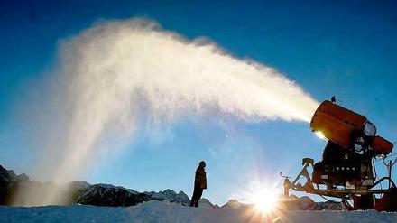Eine Schneekanone schießt in hohem Bogen Schnee in den blauen Himmel. 