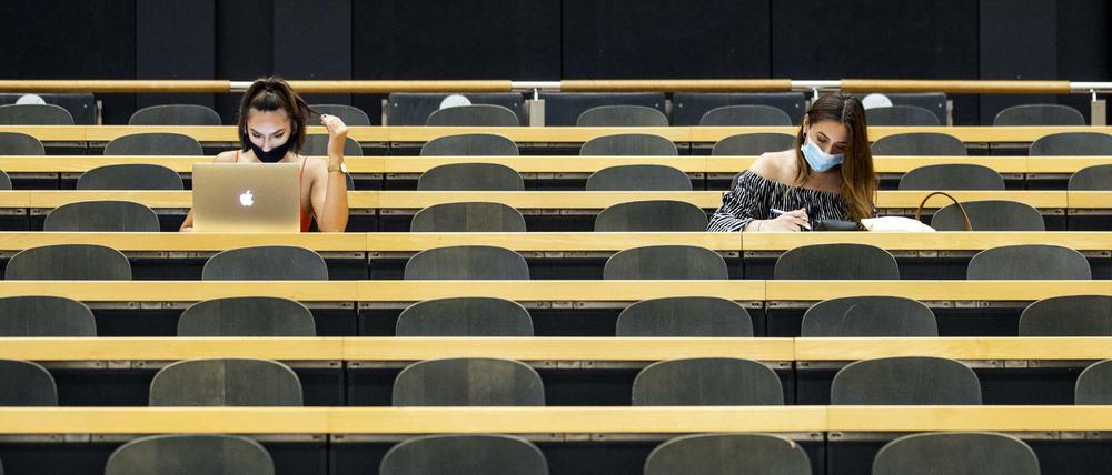 Zwei Studentinnen sitzen mit Mund-Nasen-Schutz in einem fast leeren Hörsaal.