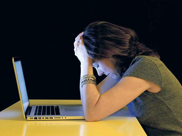 Eine junge Frau sitzt vor ihrem Laptop und stützt den Kopf in die Hände.