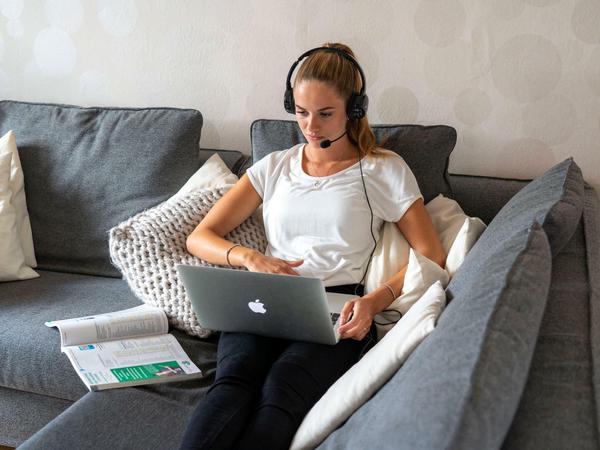 Eine Studentin sitzt zu Hause auf dem Sofa und verfolgt eine Online-Lehrveranstaltung.