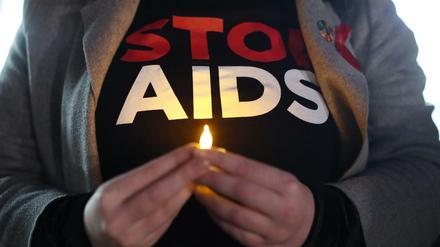 Eine Person hält ein künstliches Teelicht vor dem Körper, auf ihrem T-Shirt ist "Stop Aids" zu lesen.