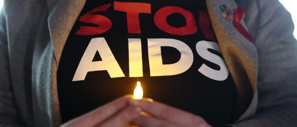 Eine Person hält ein künstliches Teelicht vor dem Körper, auf ihrem T-Shirt ist "Stop Aids" zu lesen.