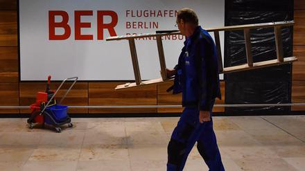 Arbeiter mit Leiter vor Flughafen-BER-Schild.