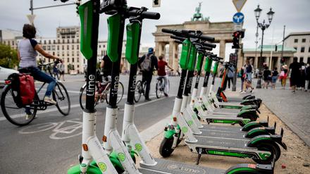 E-Tretroller stehen vor dem Brandenburger Tor am Rand der Straße des 17. Juni geparkt, während Fahrradfahrer an der Ampel warten.