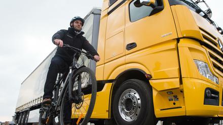 Größenunterschied: Ein Radfahrer steht mit seinem Fahrrad in der Versuchsabteilung von Mercedes Benz neben einem Lkw.