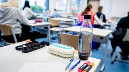 Mehrere Stifte liegen und eine Wasserflasche steht auf einem Tisch in einer Schule.