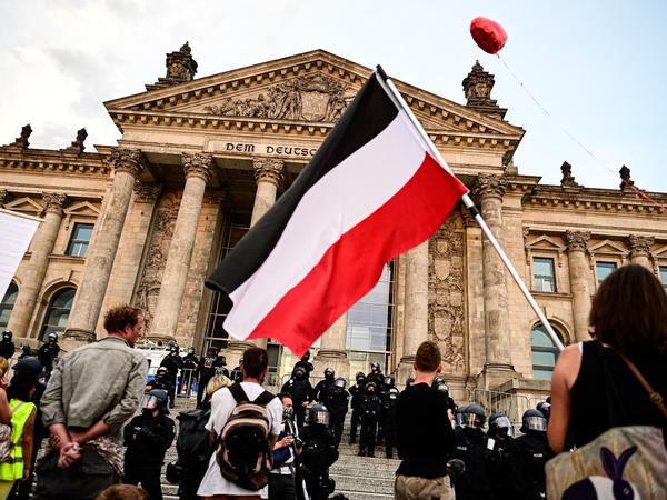 Teilnehmer bei einer Kundgebung gegen die Corona-Maßnahmen stehen vor dem Reichstag in Berlin, eine Person hält eine Reichsflagge.