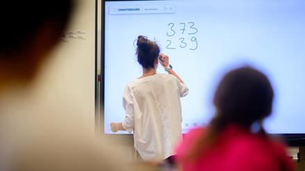 Eine Lehrerin schreibt eine Mathematikaufgabe auf eine digitale Schultafel im Klassenraum einer 4. Klasse einer Grundschule (Symbolbild).