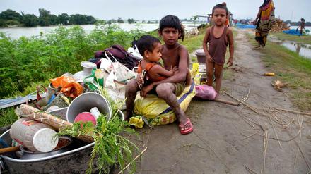Vom Hochwasser betroffene Kinder sitzen neben ihren Habseligkeiten.