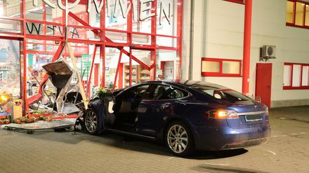 Ein Tesla steht nach einem Unfall vor dem zerstörten Eingang eines Baumarktes.