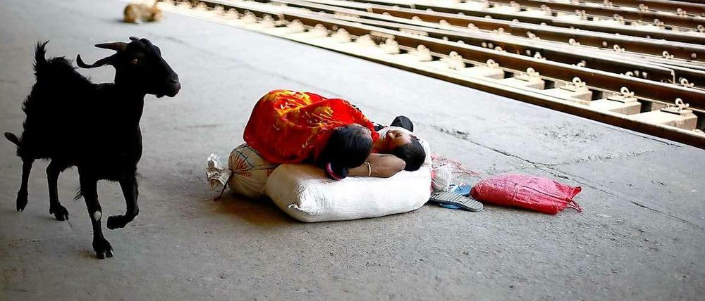 Eine Frau in Bangladesch schläft mit ihrem kleinen Sohn auf dem Bahnsteig. Eine Ziege läuft vorbei.