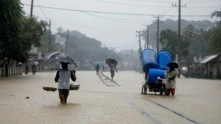 Menschen waten durch eine überschwemmte Straße in Bangladesch (Symbolbild).