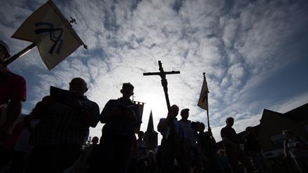 Pilger der 166. Telgter Wallfahrt gehen im Gegenlicht auf einer Straße und halten ein Kreuz.