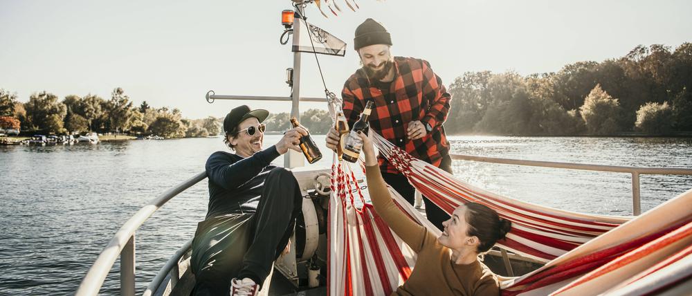 Drei Personen auf einem Boot prosten sich fröhlich mit Getränken zu.