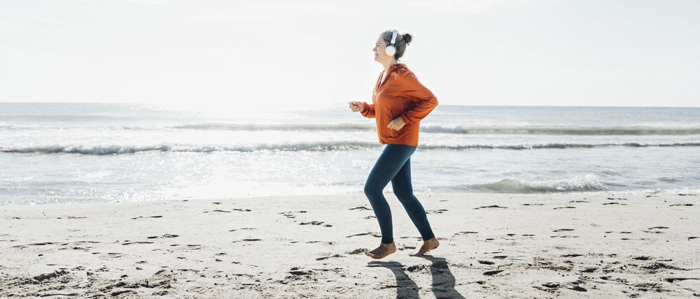 Eine junge Frau joggt barfuß am Strand entlang.