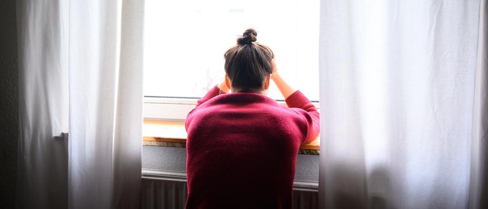 Eine Frau sitzt mit Kopf in den Händen am Fenster (Symbolbild).