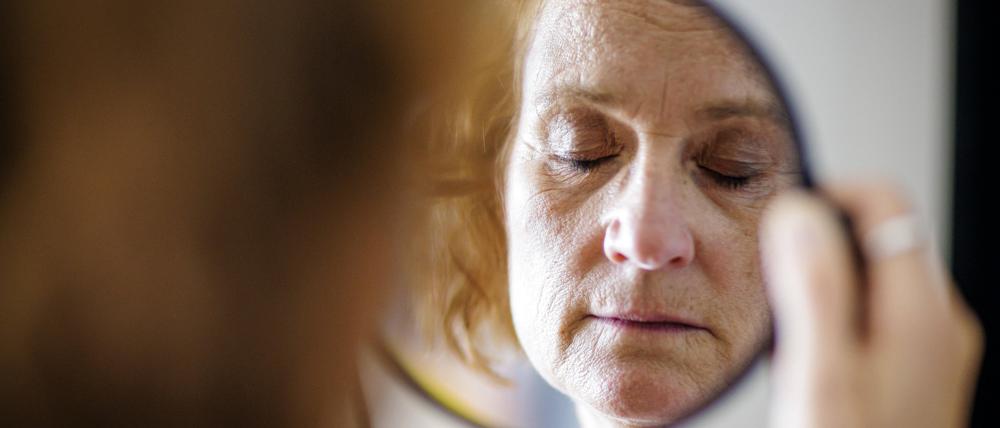 Eine ältere Frau mit geschlossenen Augen ist in einem kleinen Handspiegel zu sehen.