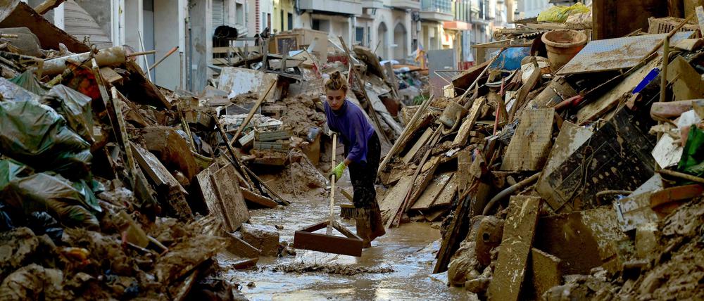 Eine Frau in Paiporta bei Valencia versucht, Schlamm aus der überfluteten Straße zu entfernen.