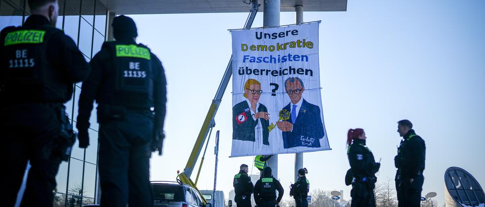 Polizeibeamte am Paul-Löbe-Haus neben dem Protestbanner eines Künstlerkollektivs, das gemalte Bilder von Alice Weidel, Kanzlerkandidatin und Fraktionsvorsitzende der AfD, und Friedrich Merz, Unions-Kanzlerkandidat und CDU-Bundesvorsitzender, zeigen soll.