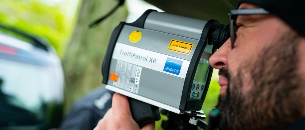 Ein Polizist kontrolliert mit einem Messgerät die Geschwindigkeit von Fahrzeugen in einer 30er-Zone.