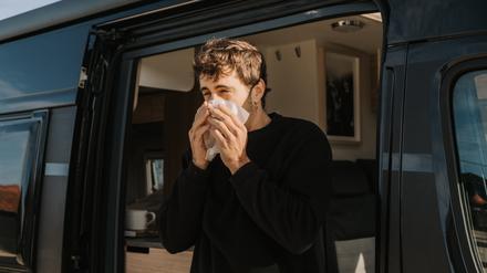 Ein Mann steht in der Tür eines Wohnmobils und schnaubt in ein Taschentuch.