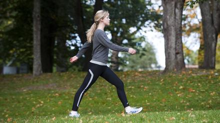 Eine Frau geht schnellen Schrittes durch einen Park.