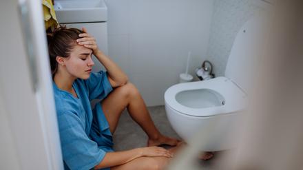 Eine junge Schwangere sitzt vor einer Toilette..