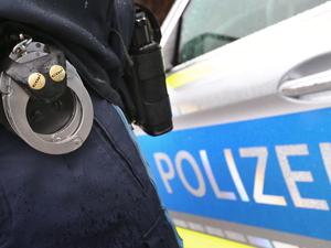 Ein Polizist mit Handschellen und einer Pistole am Gürtel steht vor einem Streifenwagen.