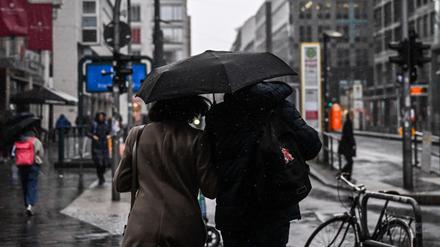 Passanten auf der Friedrichstraße teilen sich einen Regenschirm.